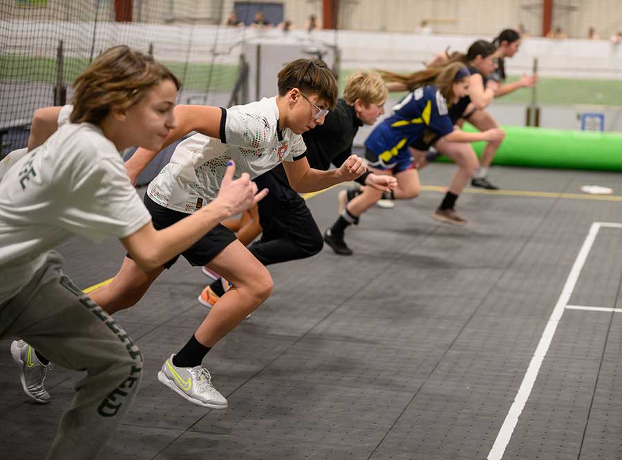 A line of players sprinting from a standing start during a speed drill on the indoor court at Allsport Arena.